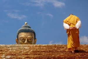 A Buddhist monk in traditional wear ascending stairs towards a large Buddha statue, symbolizing spirituality.